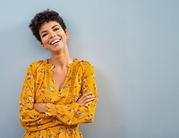 A smiling middle-aged woman standing against a wall with her arms crossed.